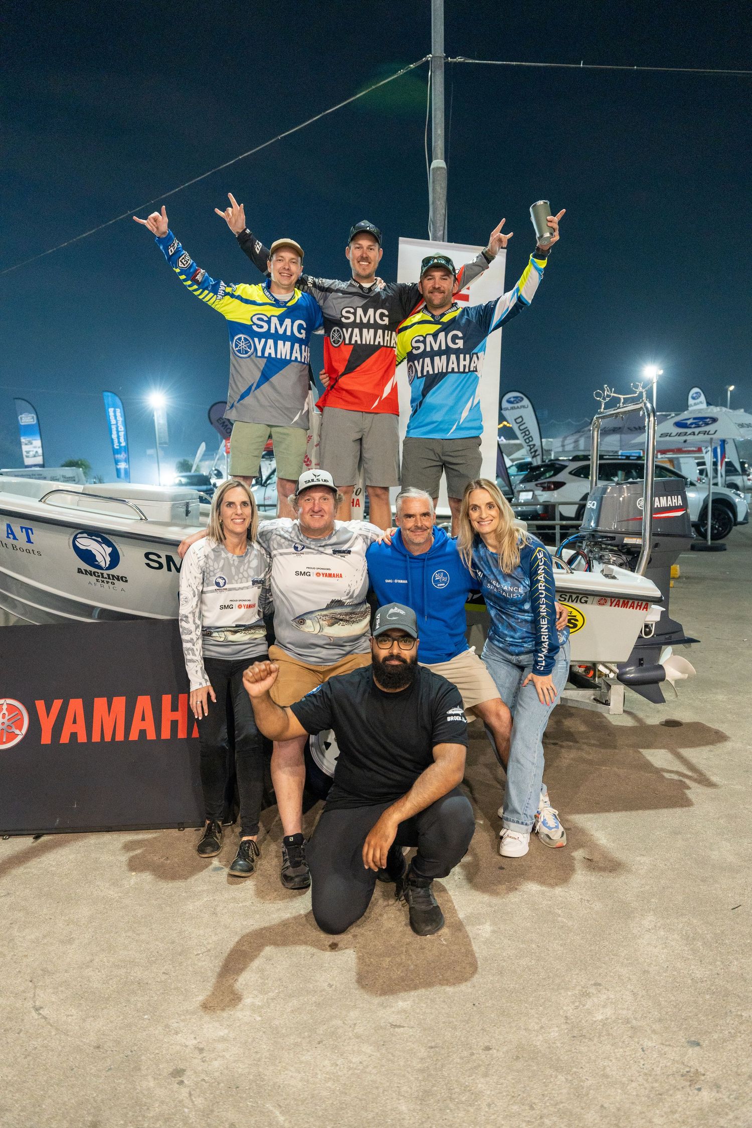 Group photo of people posing with a fishing boat, some standing on the boat and others in front.
