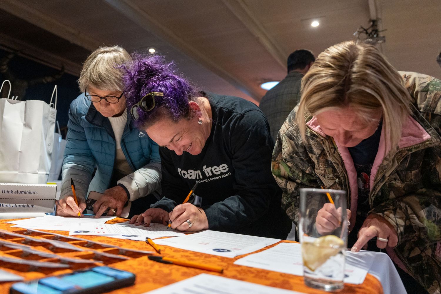 People writing or signing documents at a table during a fly fishing event.