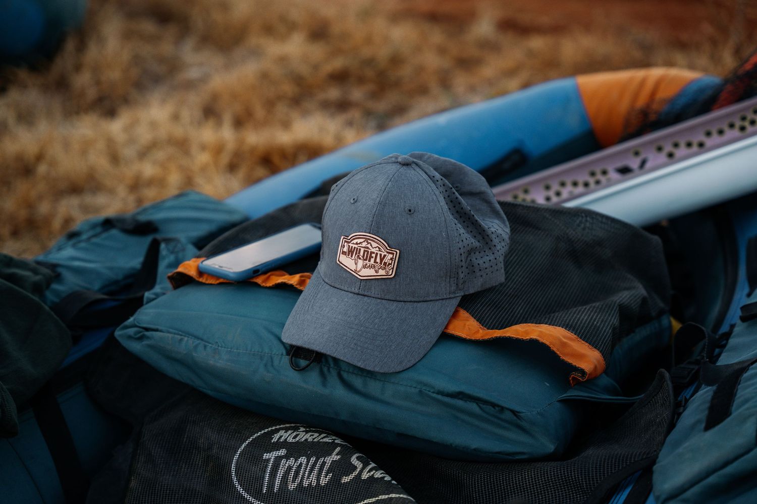 Blue and black fishing gear bag with worn baseball cap on ground.