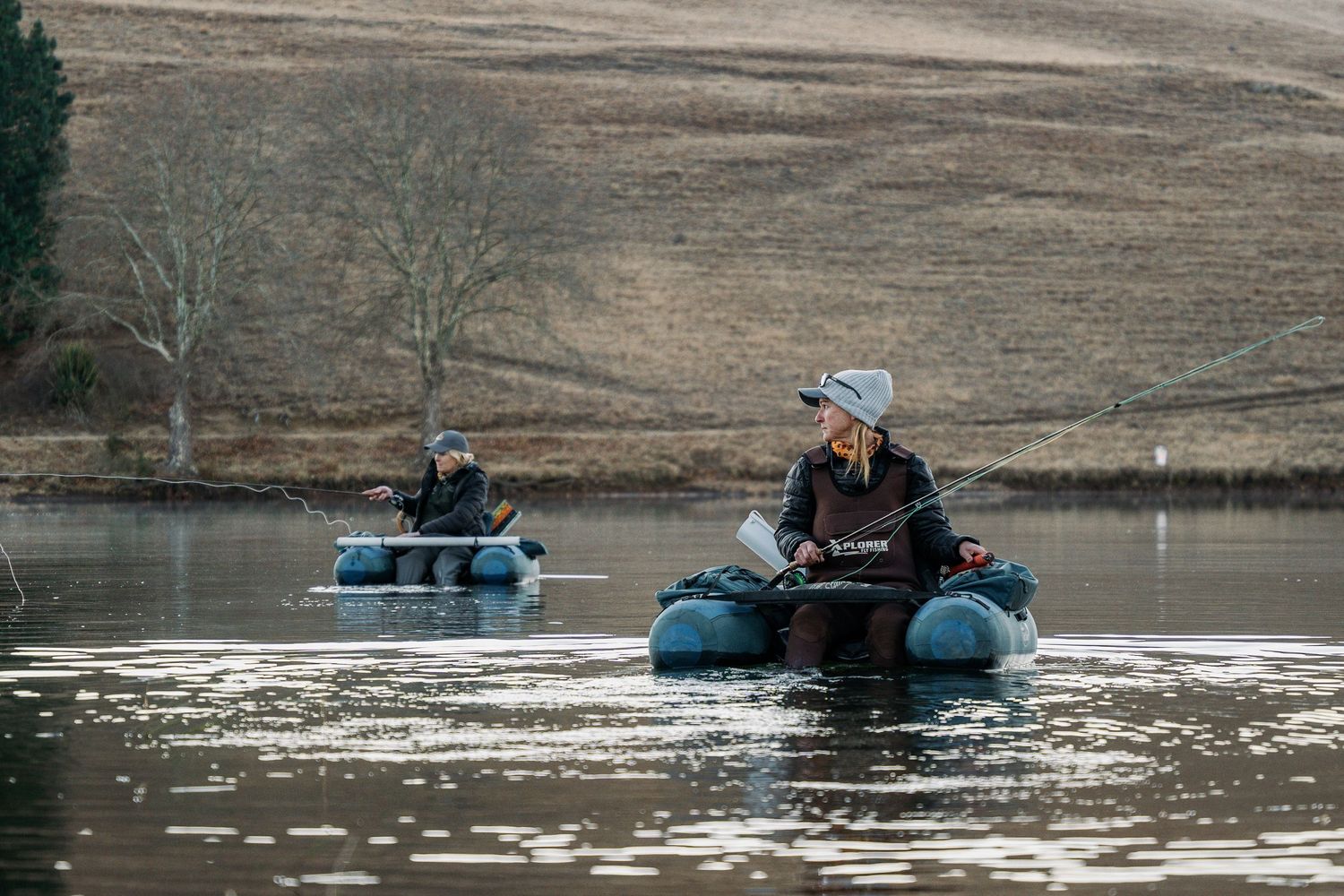 Anglers in float tubes fishing on calm winter lake.