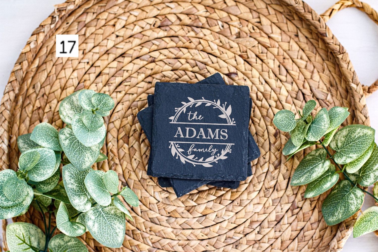 Custom Adams family slate coaster centered on natural woven placemat with faux greenery.