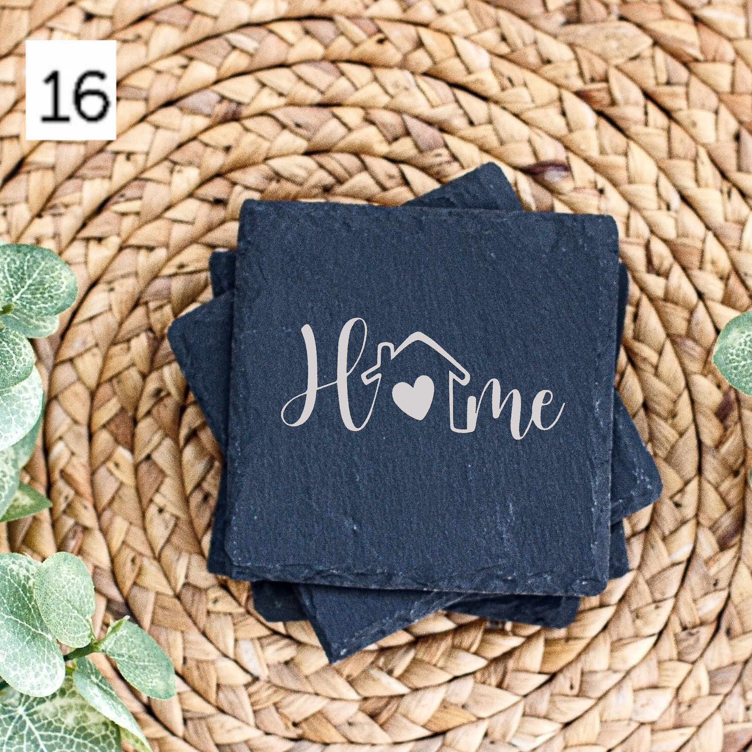 Decorative slate coaster with 'Home' text on woven rattan mat with artificial green leaves.