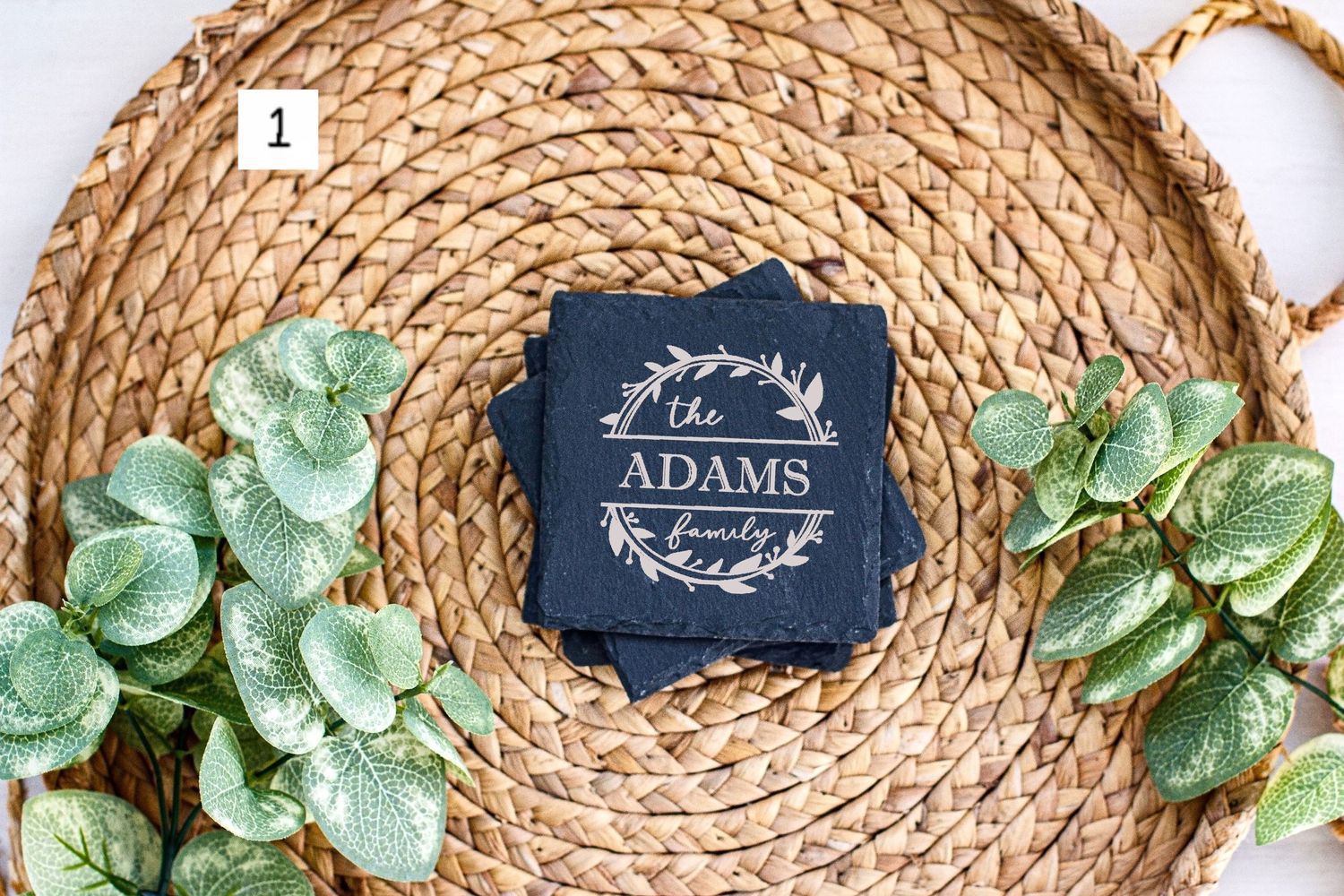 Custom family name tag in navy blue displayed on circular woven mat with decorative greenery.
