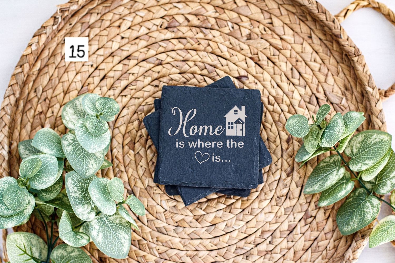 Navy blue home-themed coaster displayed on circular woven mat with green foliage accents.