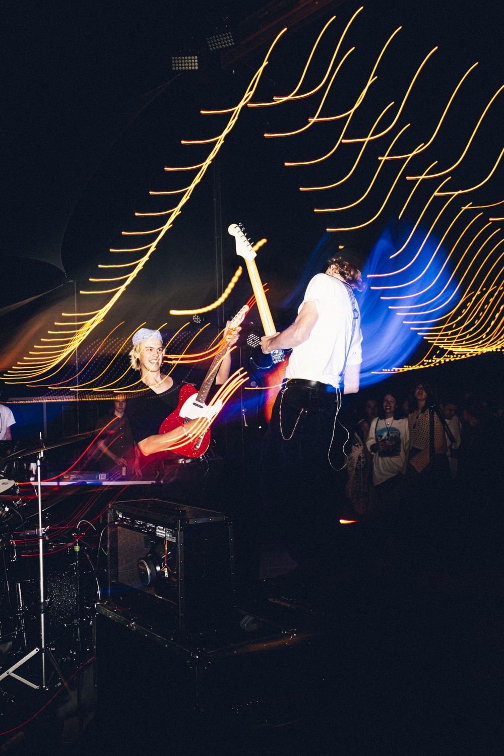 Musicians on stage with curved light trails creating dynamic visual patterns in background.