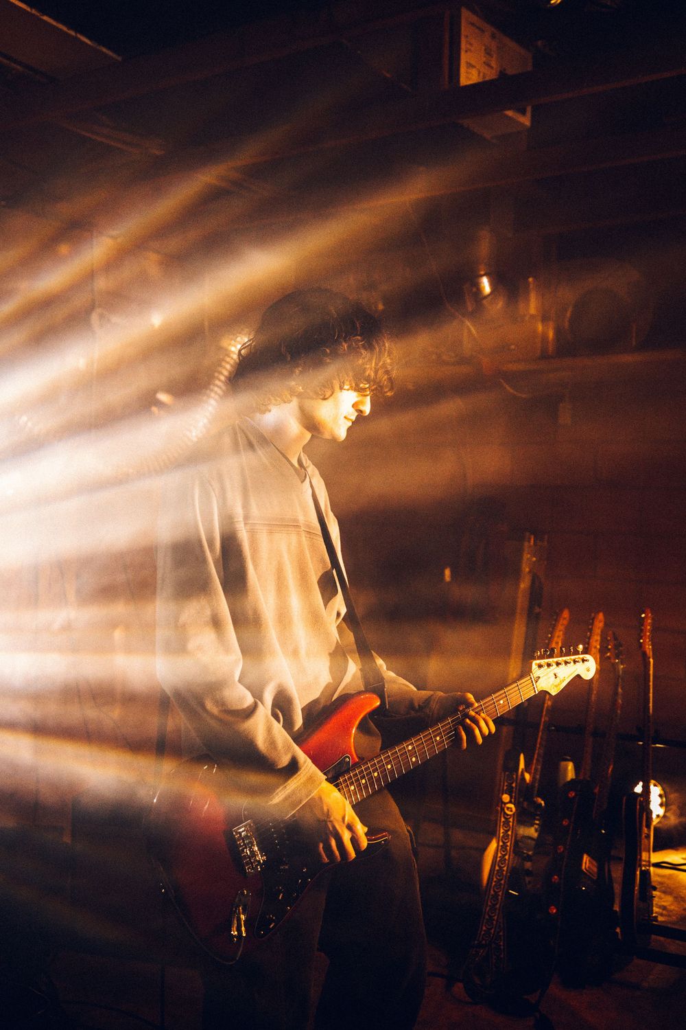A guitarist performs on stage silhouetted against dramatic orange spotlights creating atmospheric beams through smoke.