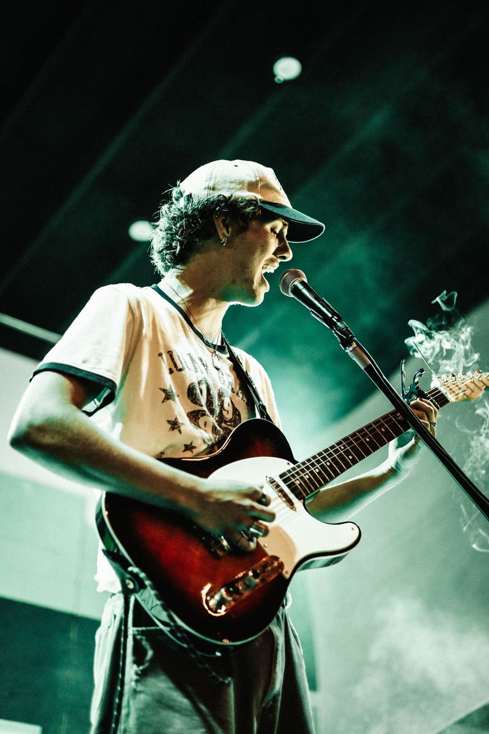 A guitarist performs on stage bathed in dramatic green lighting and fog effects during a live concert performance.