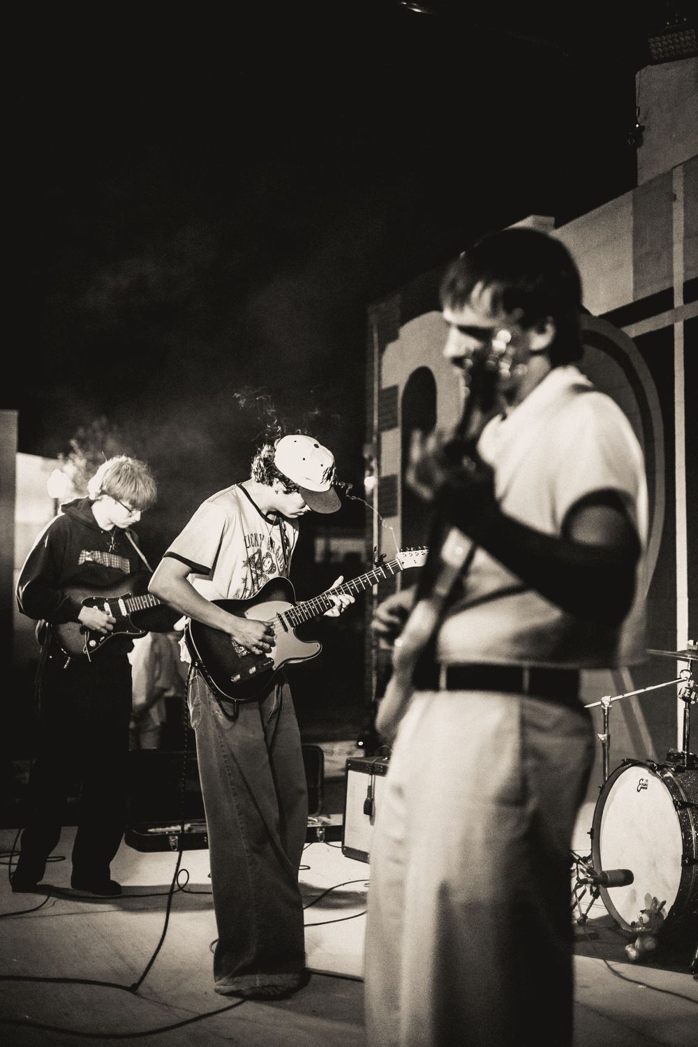 Musicians perform on stage in a dimly lit venue, captured in a black and white photo series.