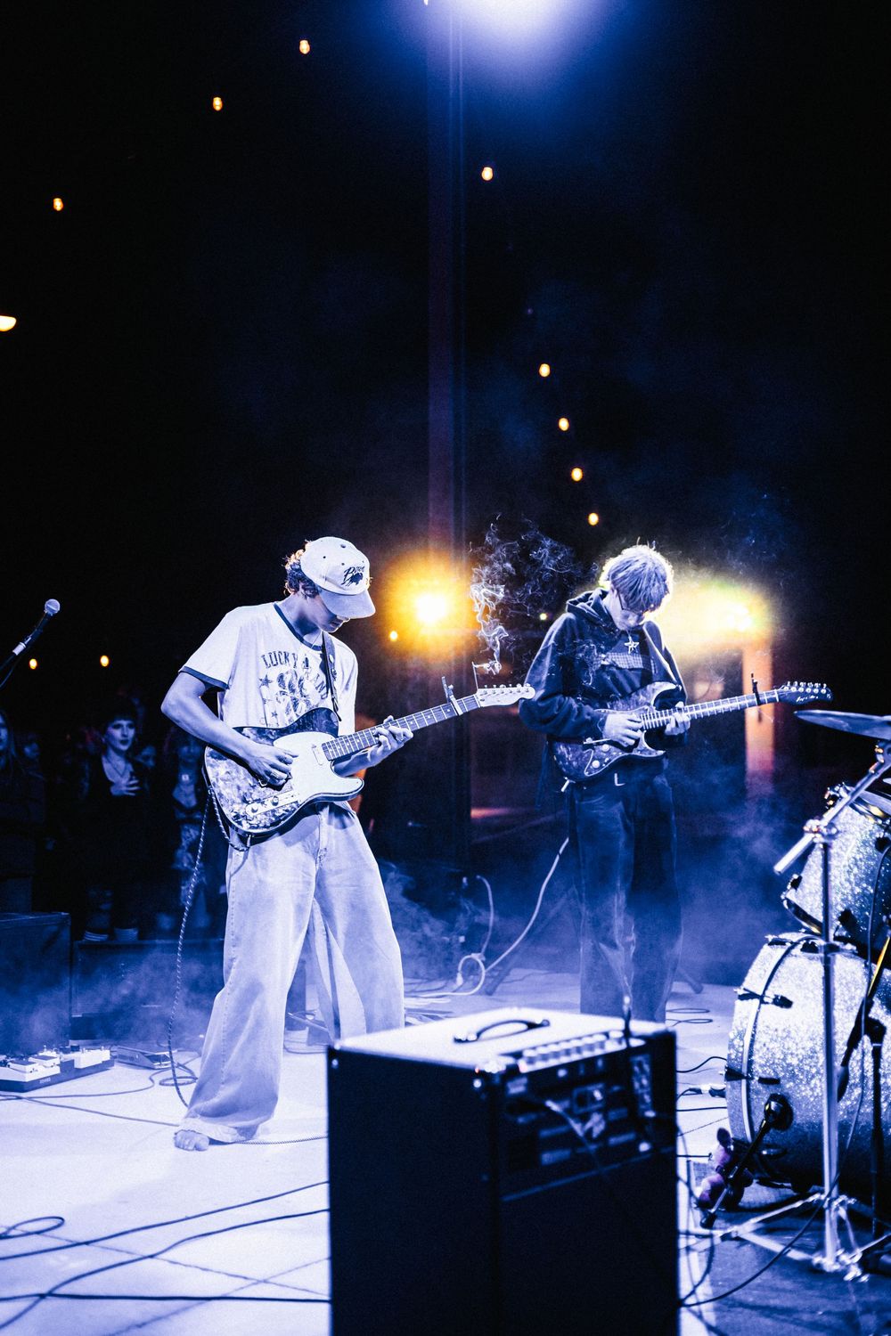 Musicians perform on stage with blue lighting and fog effects during a nighttime concert performance.