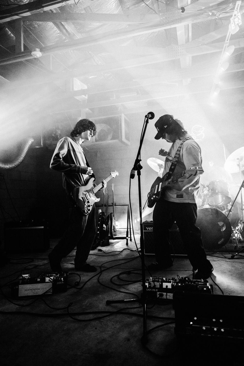 Black and white concert photo showing musicians performing on stage in dramatic lighting and fog.