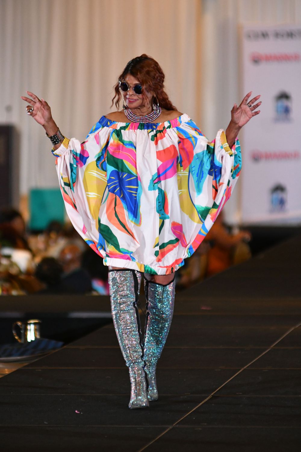 Model wears colorful oversized patterned tunic with metallic leggings on fashion runway.