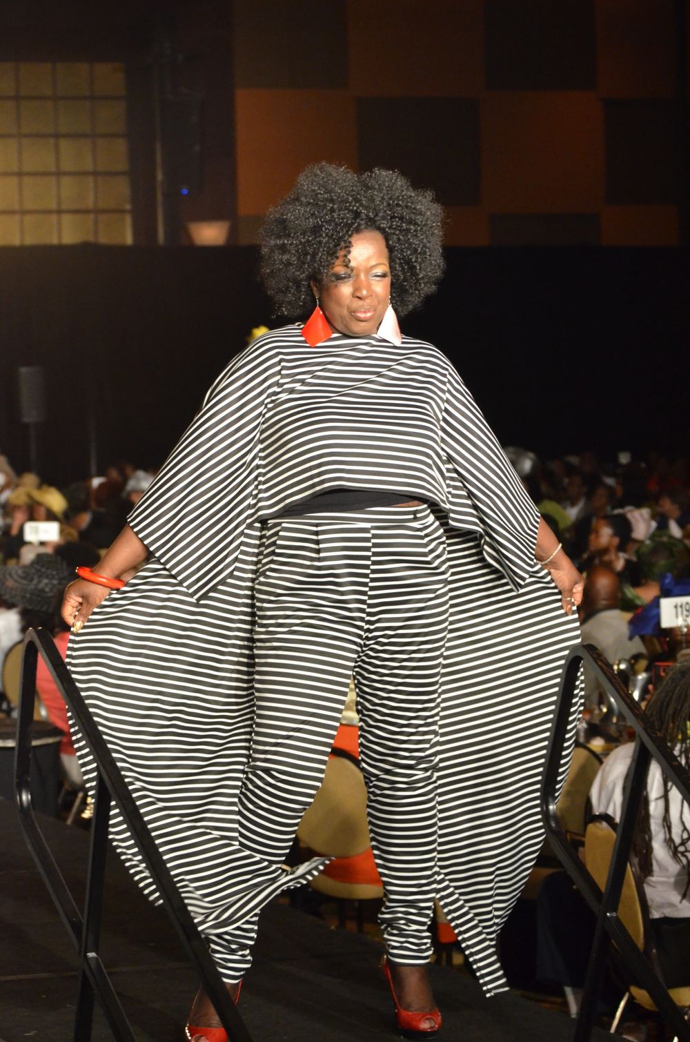Model showcases dramatic striped kaftan with voluminous silhouette on fashion runway.