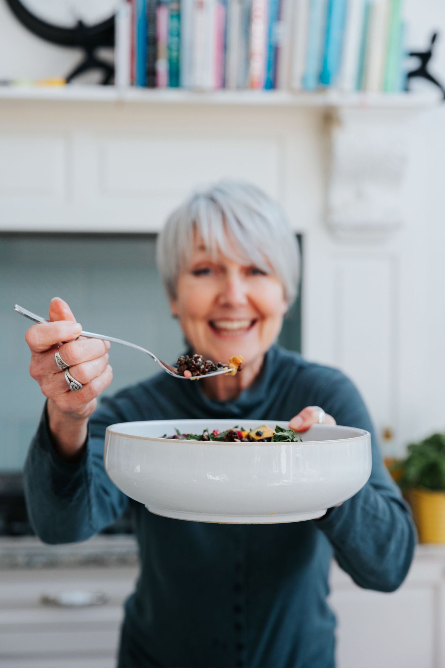 Someone holding a large white bowl and smiling while enjoying a healthy meal in a bright kitchen.