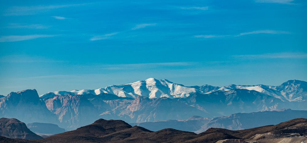 Snow-capped mountain peaks rise above misty valleys under a bright blue sky.
