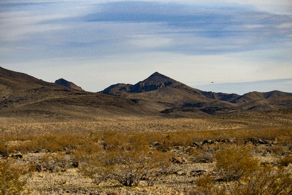 Desert mountains rise from the golden desert floor under wispy clouds in the American Southwest.