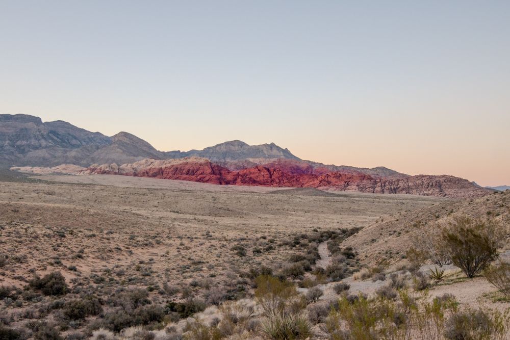 Red rock cliffs and desert terrain stretch across the landscape at sunset.