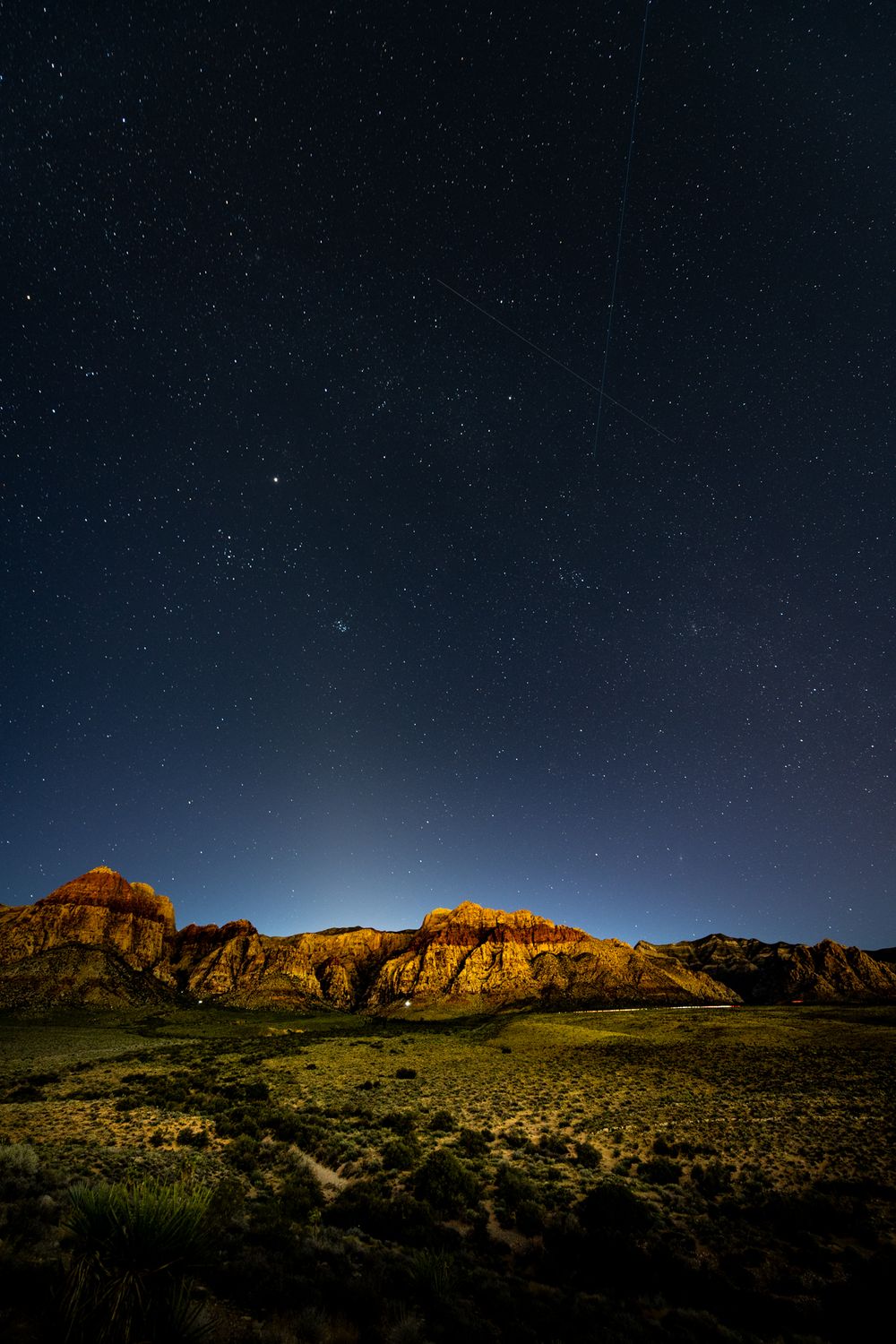 Red rock formations glow under a starry night sky in the desert landscape.
