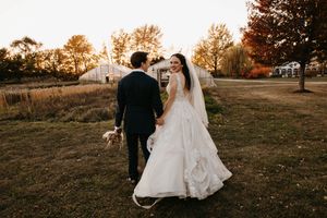 Bride and groom walk hand in hand through golden field at sunset on wedding day.