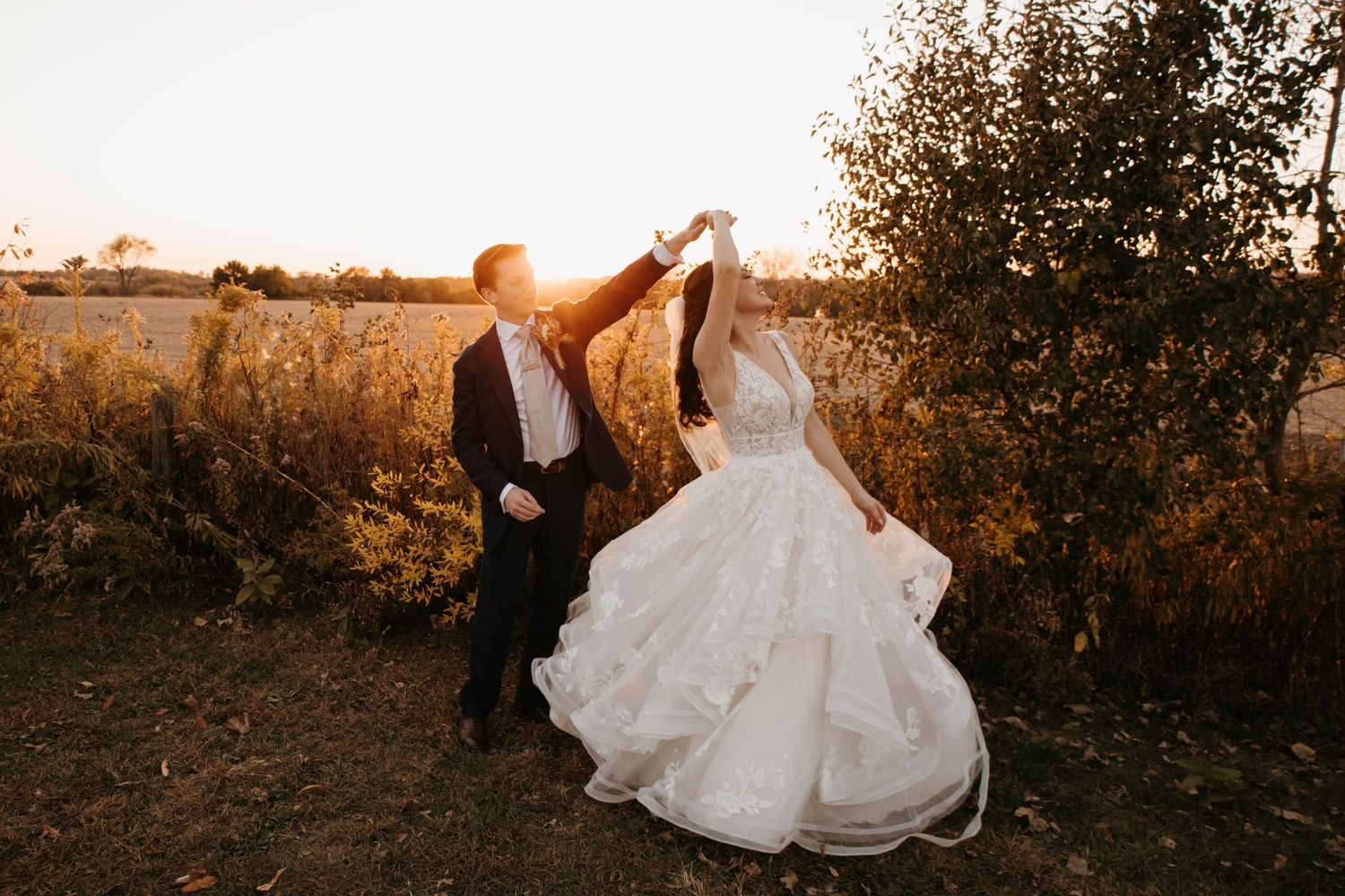 Bride and groom dancing at golden hour in a field, groom twirling bride in a stunning white ball gown.