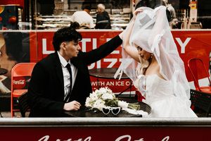 Bride and groom share playful moment at outdoor pizza shop table on wedding day.