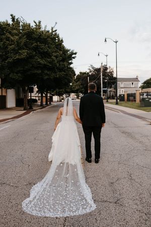Bride and groom walking away down an empty street, bride's floral cathedral veil trailing behind.