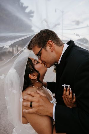 Bride and groom sharing a romantic kiss under the bride's flowing floral-embroidered wedding veil.