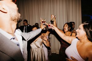 Wedding guests raise glasses in a joyful toast during lively evening reception celebration.