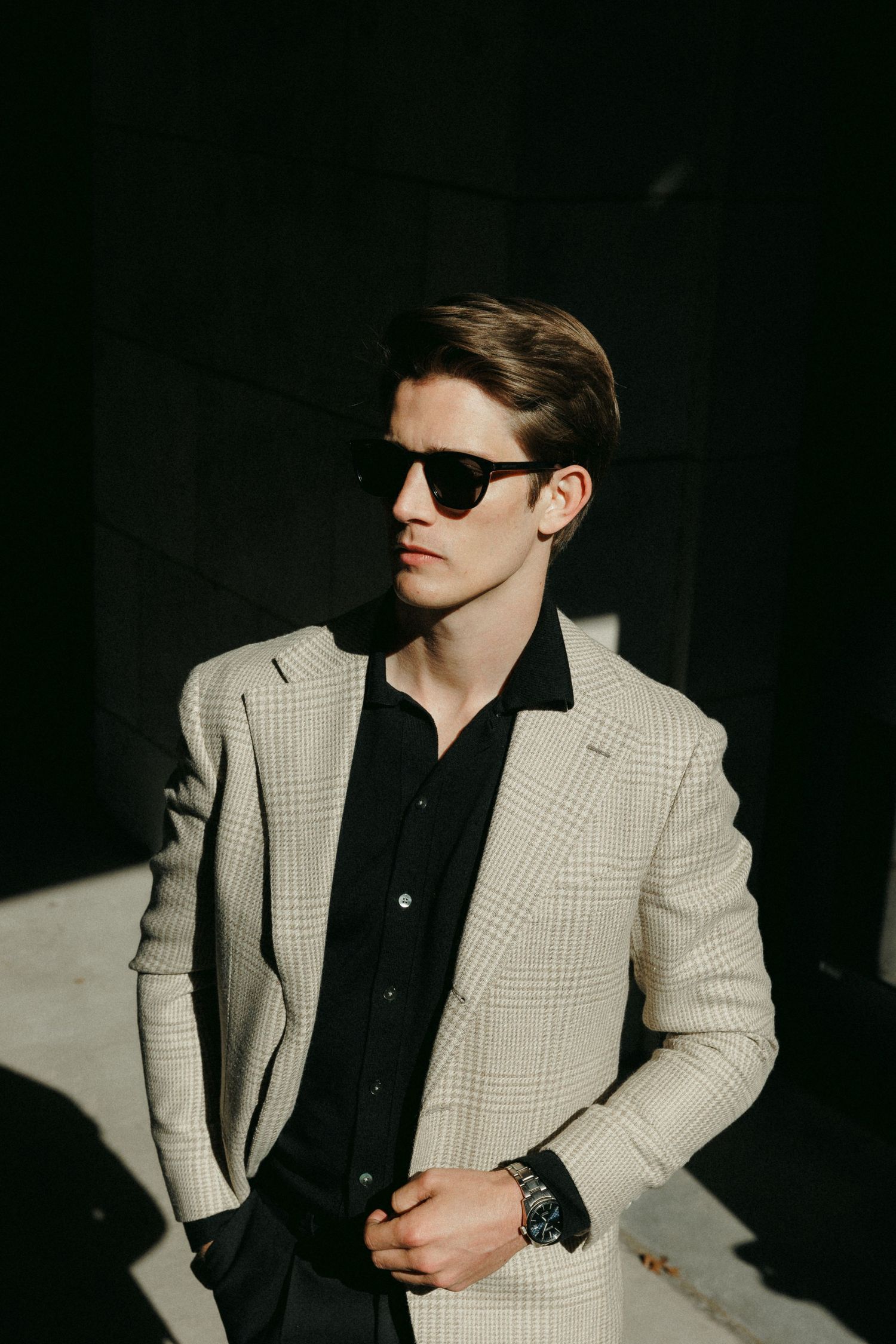 Stylish fashion portrait of person wearing checkered blazer, black shirt and sunglasses in dramatic lighting.