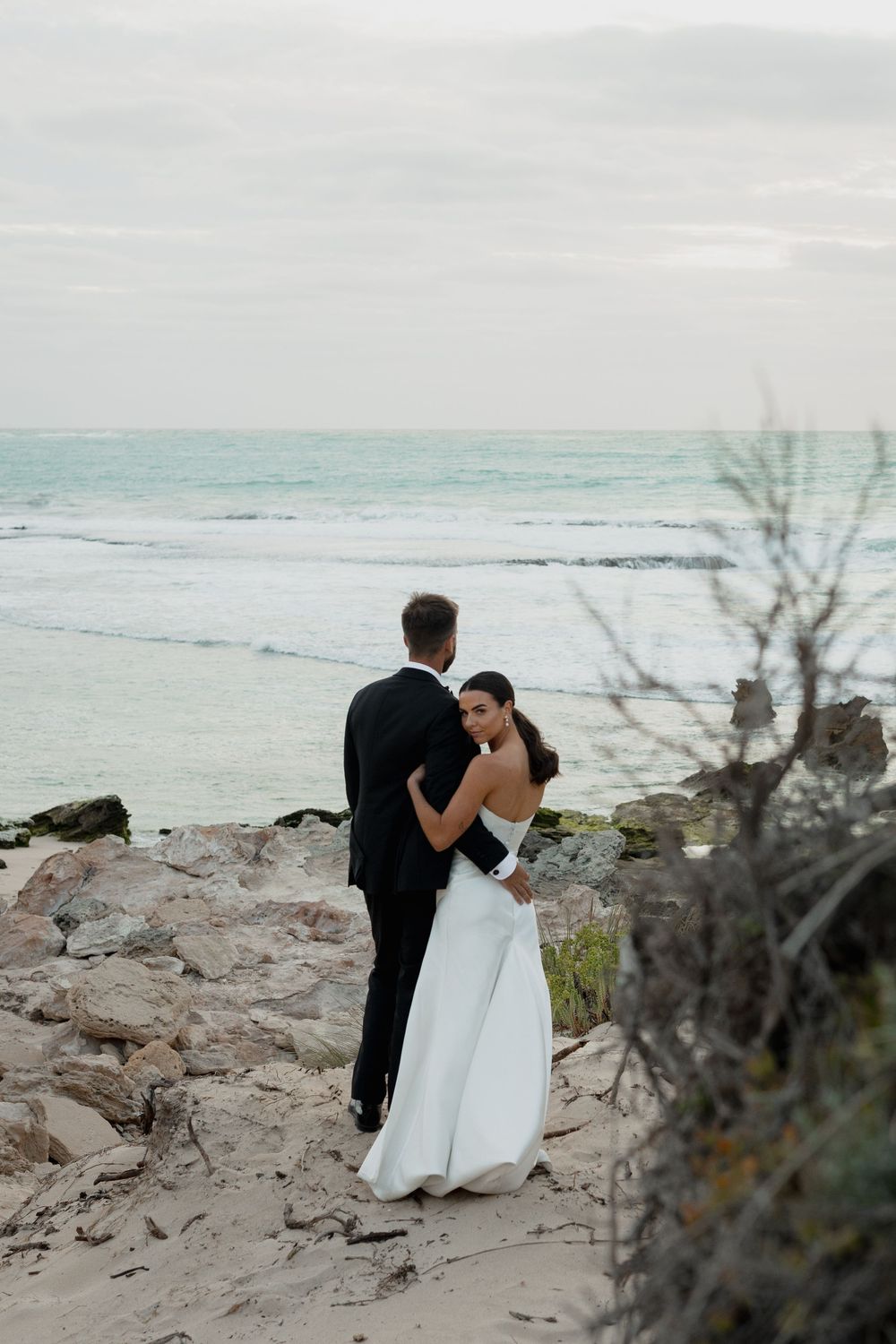 A couple shares an intimate moment on rocky coastal cliffs overlooking turquoise waters.