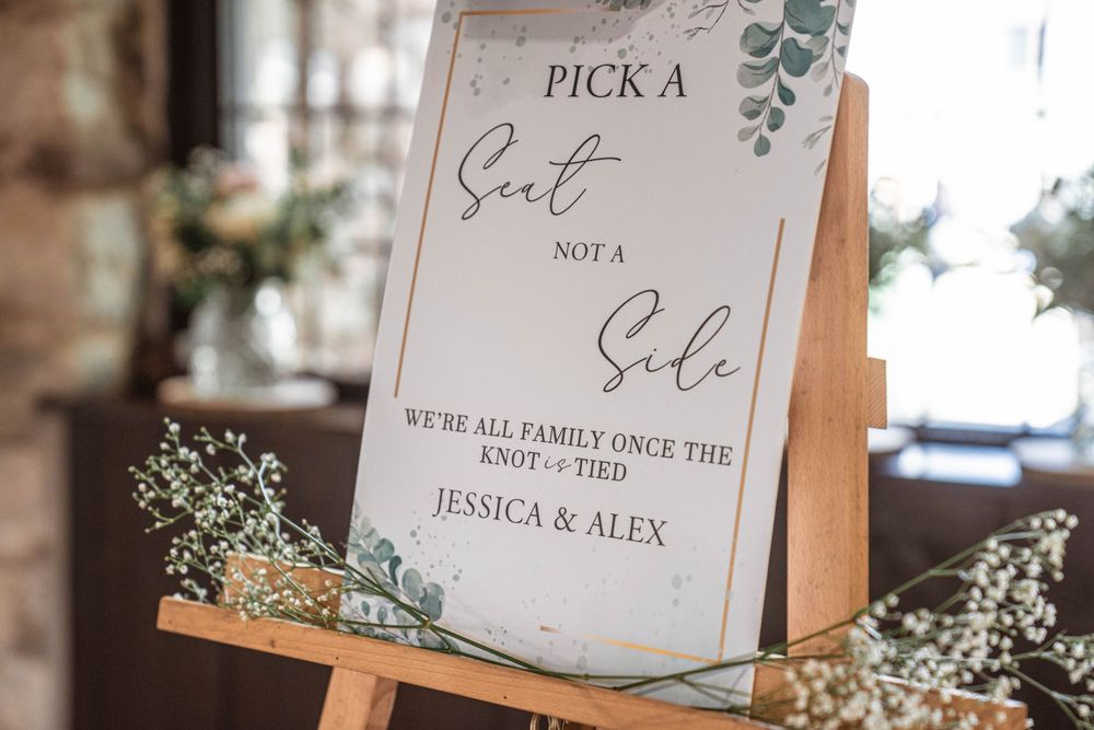 Wedding seating sign displayed on wooden easel with greenery decor.