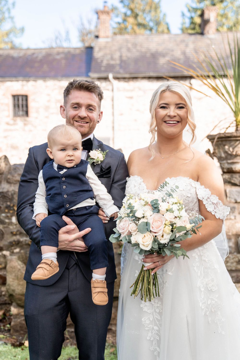Joyful wedding party portrait outside historic stone building.
