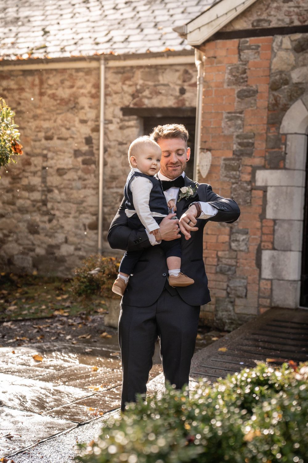 Formal wedding portrait against rustic stone building backdrop.