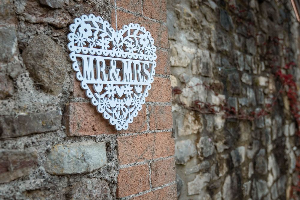 Decorative white lace heart designs and 'Mr & Mrs' text adorn a rustic stone wall at a wedding venue.