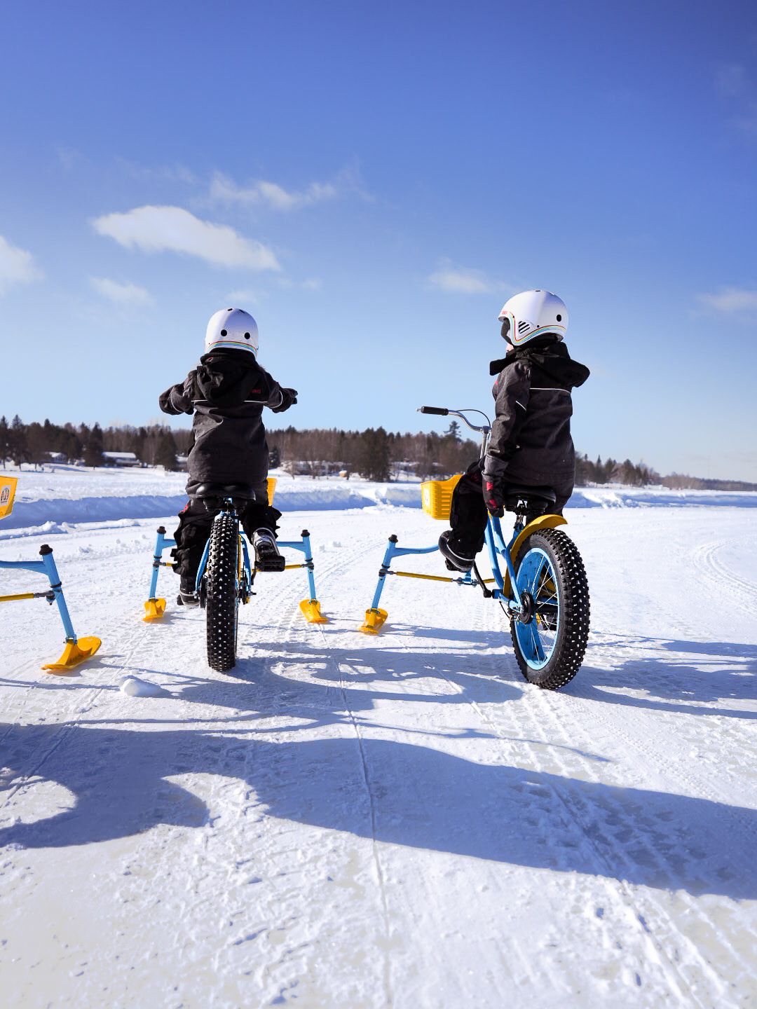 Multiple snow bikes in action on a frozen lake during a bright winter day.