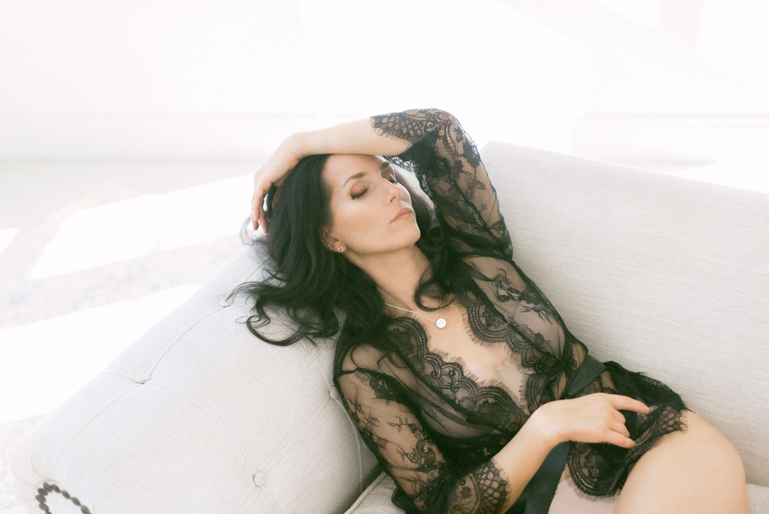 Artistic boudoir photo of someone in black lace lingerie posing against a white backdrop.