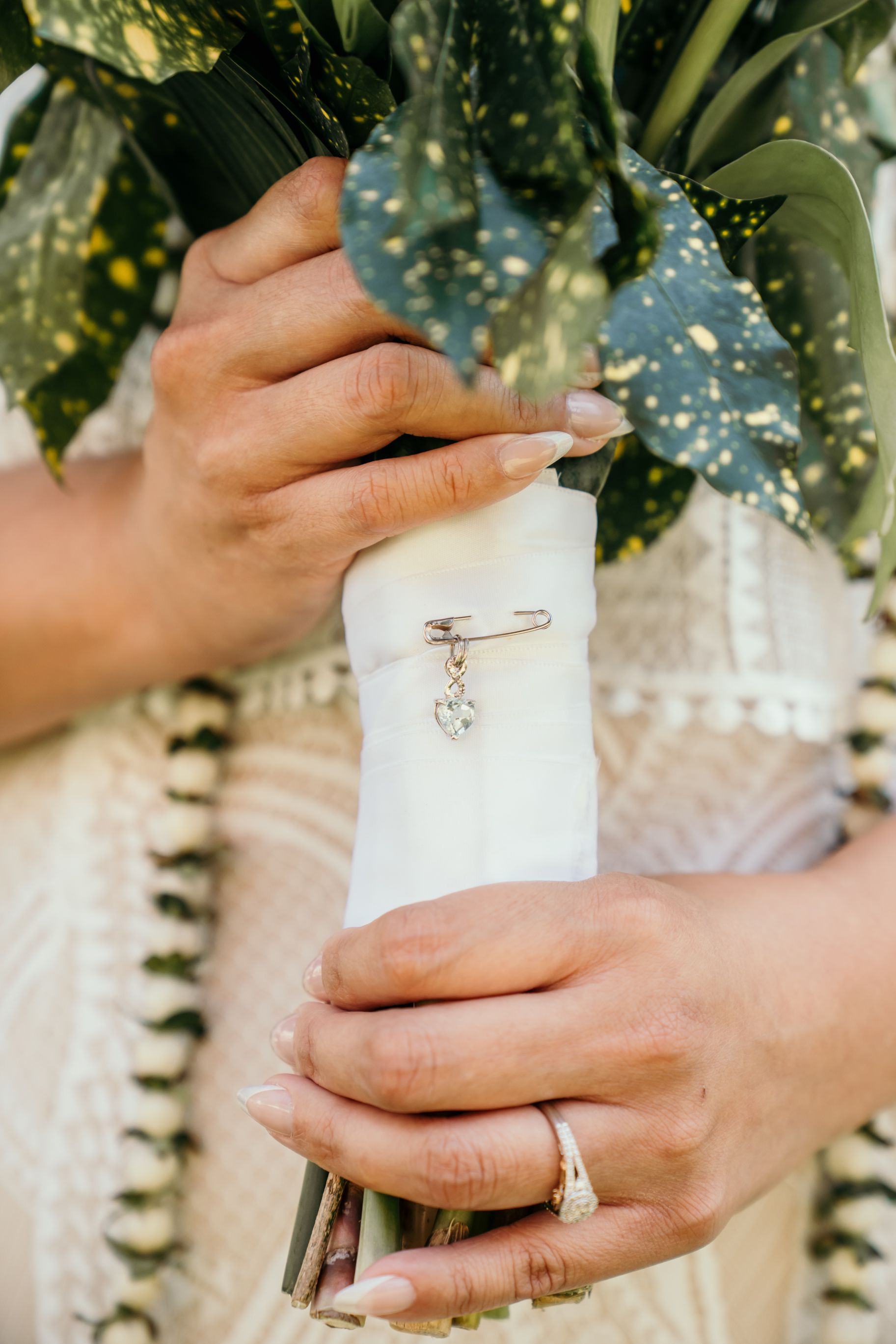 Close-up of hands holding a white-wrapped bouquet with engagement and wedding rings visible.