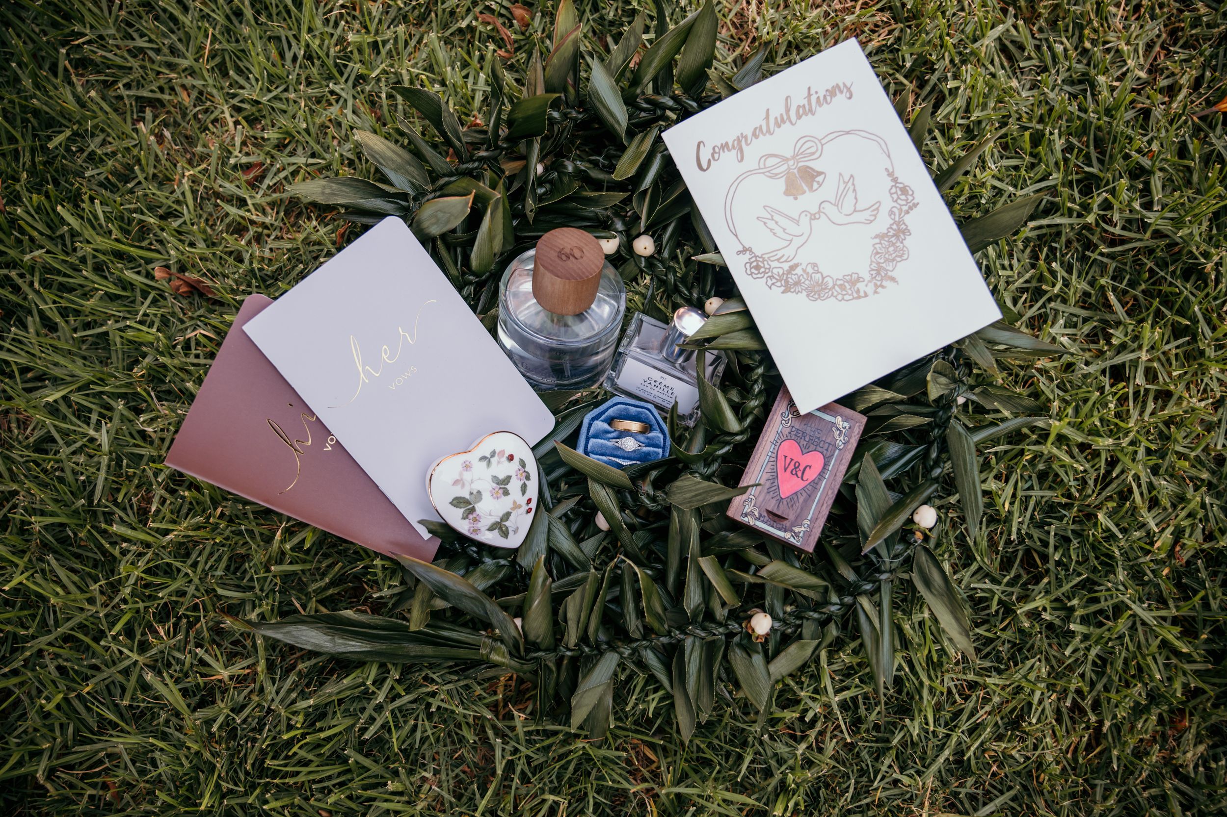 Wedding stationery and invitation cards with delicate pink floral designs arranged on grass with rings and bottles.