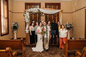 Wedding party stands together under a floral arch in an intimate indoor ceremony venue.