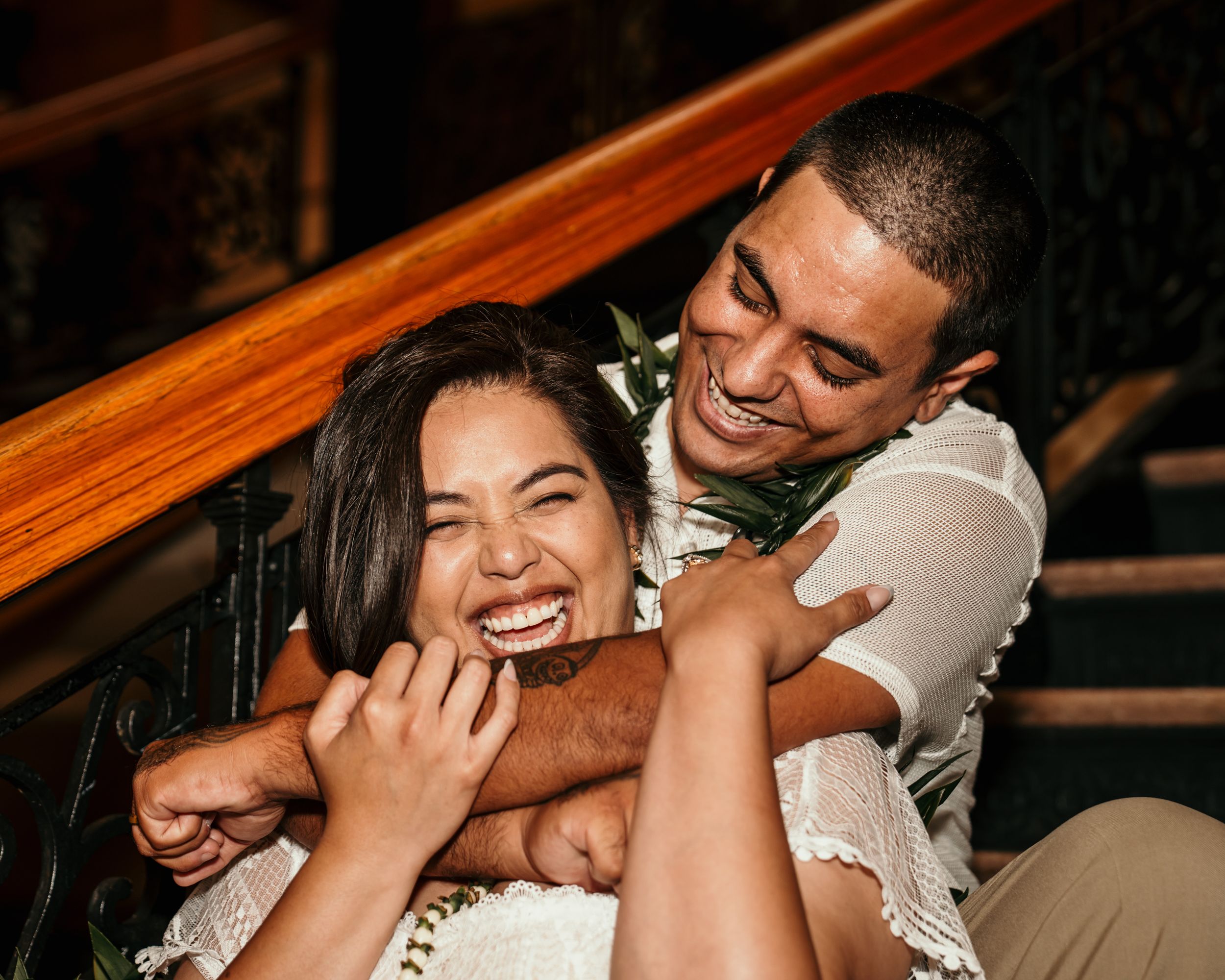 Candid moment of newlyweds sharing laughter on a wooden staircase.