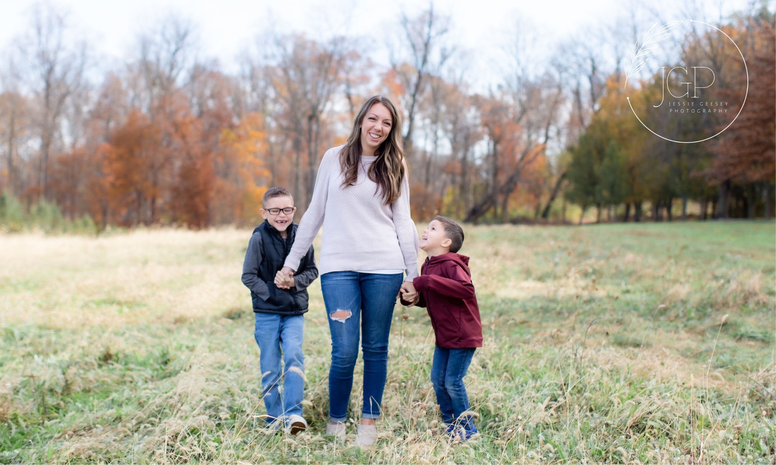 Woman holding hands with two small children in a field with fall foliage