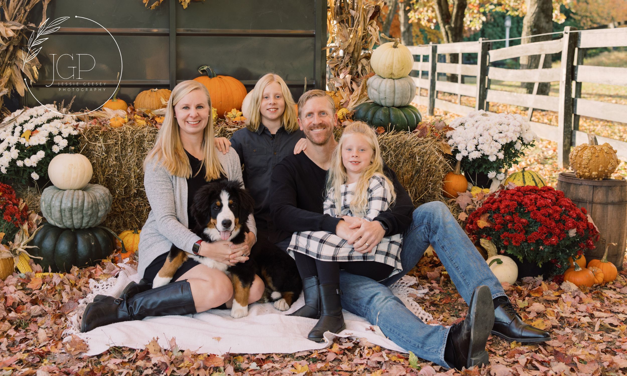 A man, woman, two children and a dog posing in front a fall backdrop