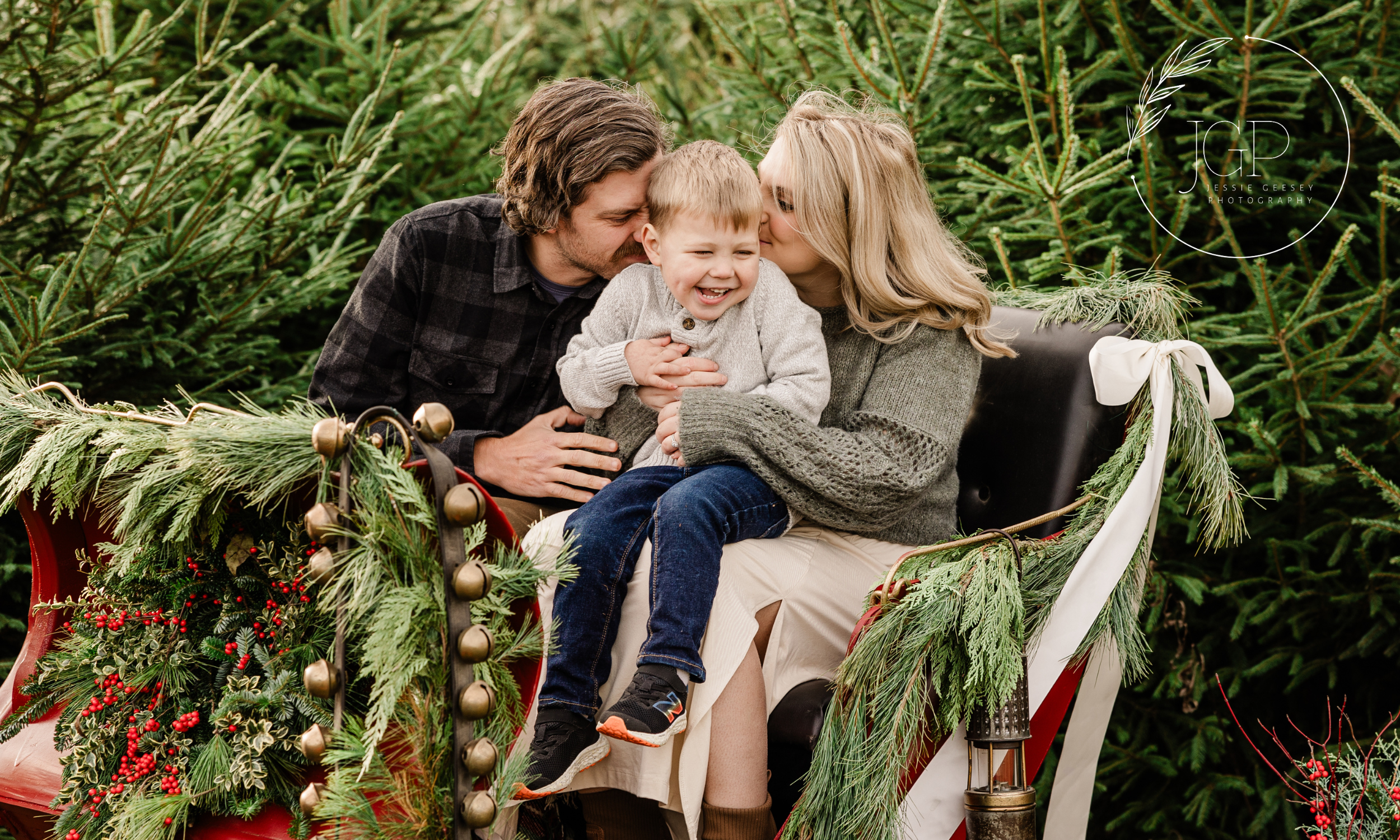A man, woman and child snuggling on a holiday sleigh covered in bells, holly and greenery