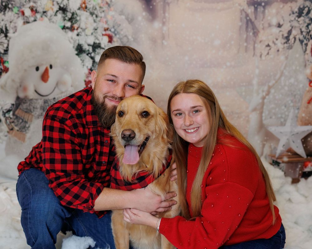 A golden retriever dog poses with people wearing red plaid flannel shirts in a holiday-themed photo session.