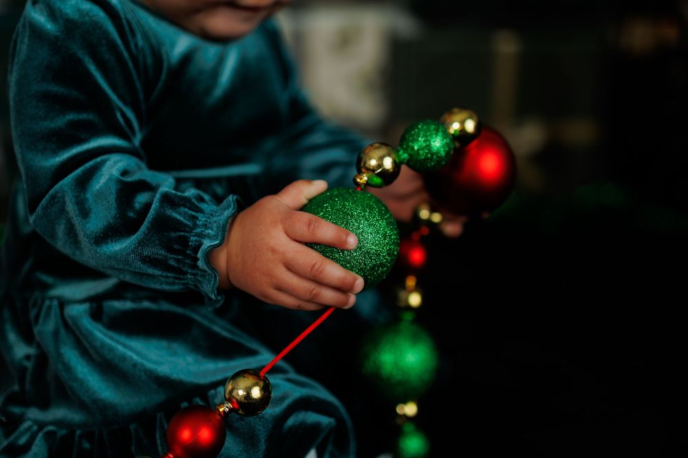 Someone's hands hold colorful red and green Christmas ornaments against a dark background.