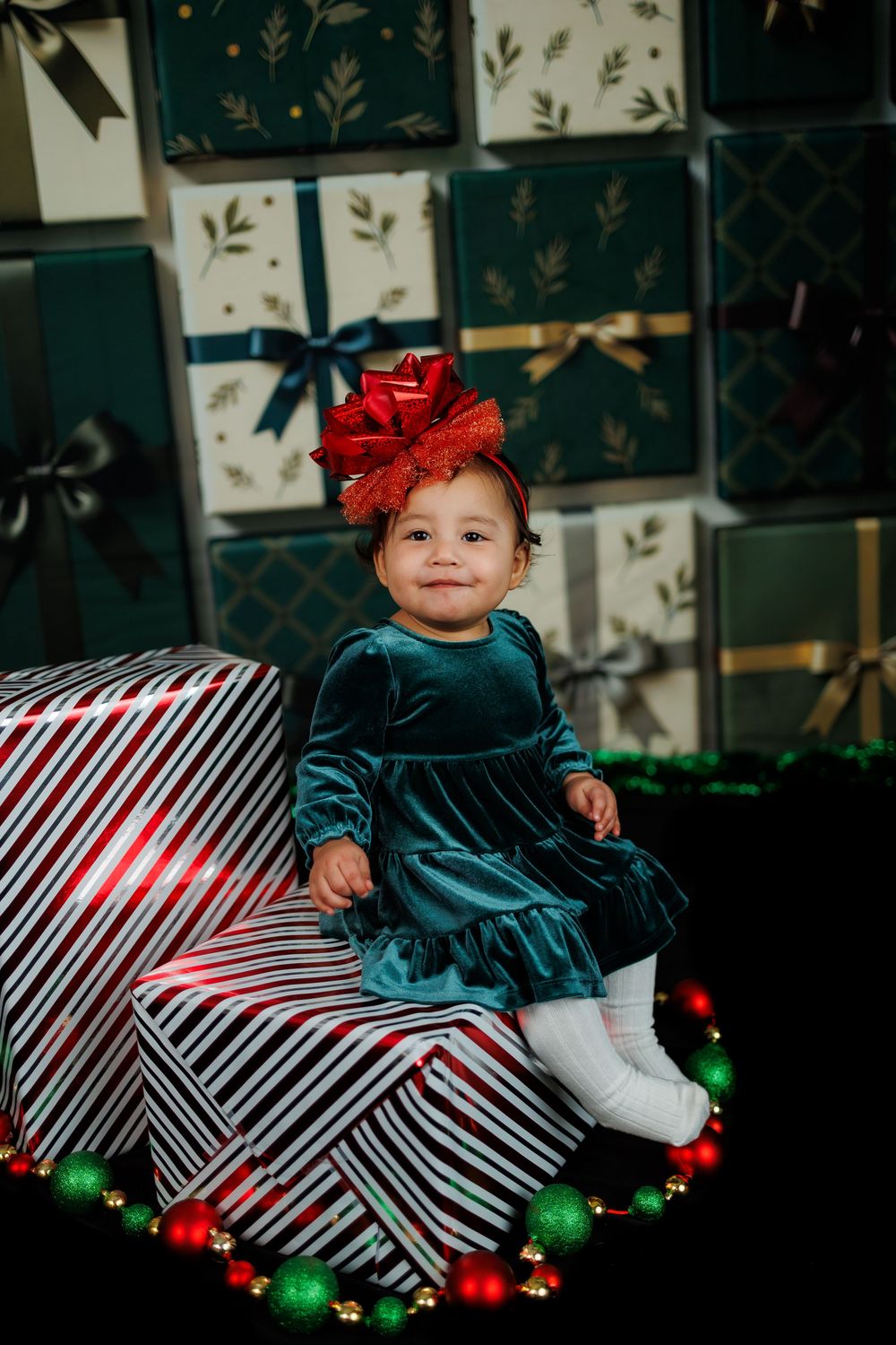 Holiday portrait with a dark dress and red bow surrounded by striped gift boxes and festive ornaments.