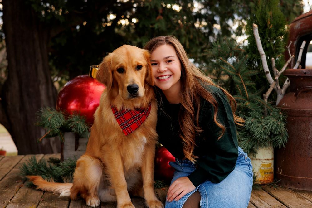 Golden retriever and companion sit together outdoors among autumn decorations and pumpkins.
