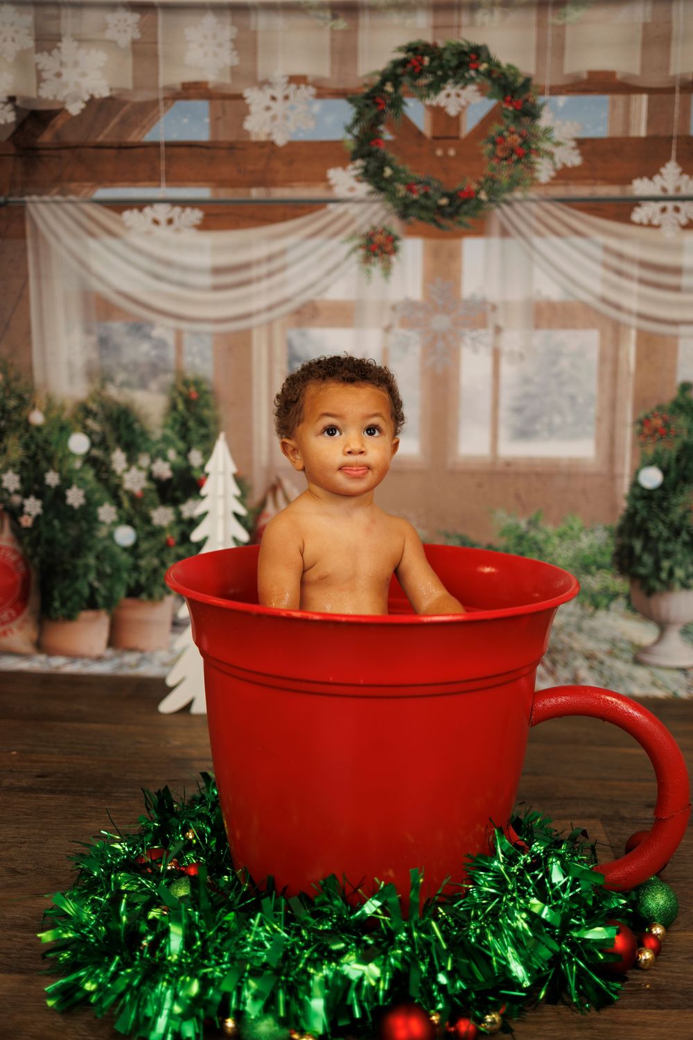 A festive holiday photo series showing a baby sitting in a large red teacup surrounded by Christmas decorations and garland.
