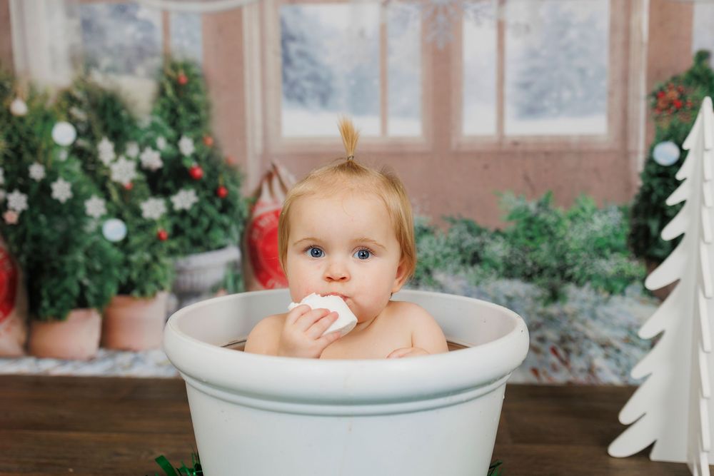 Baby taking a bath in vintage white tub with greenery and holiday decor in background.