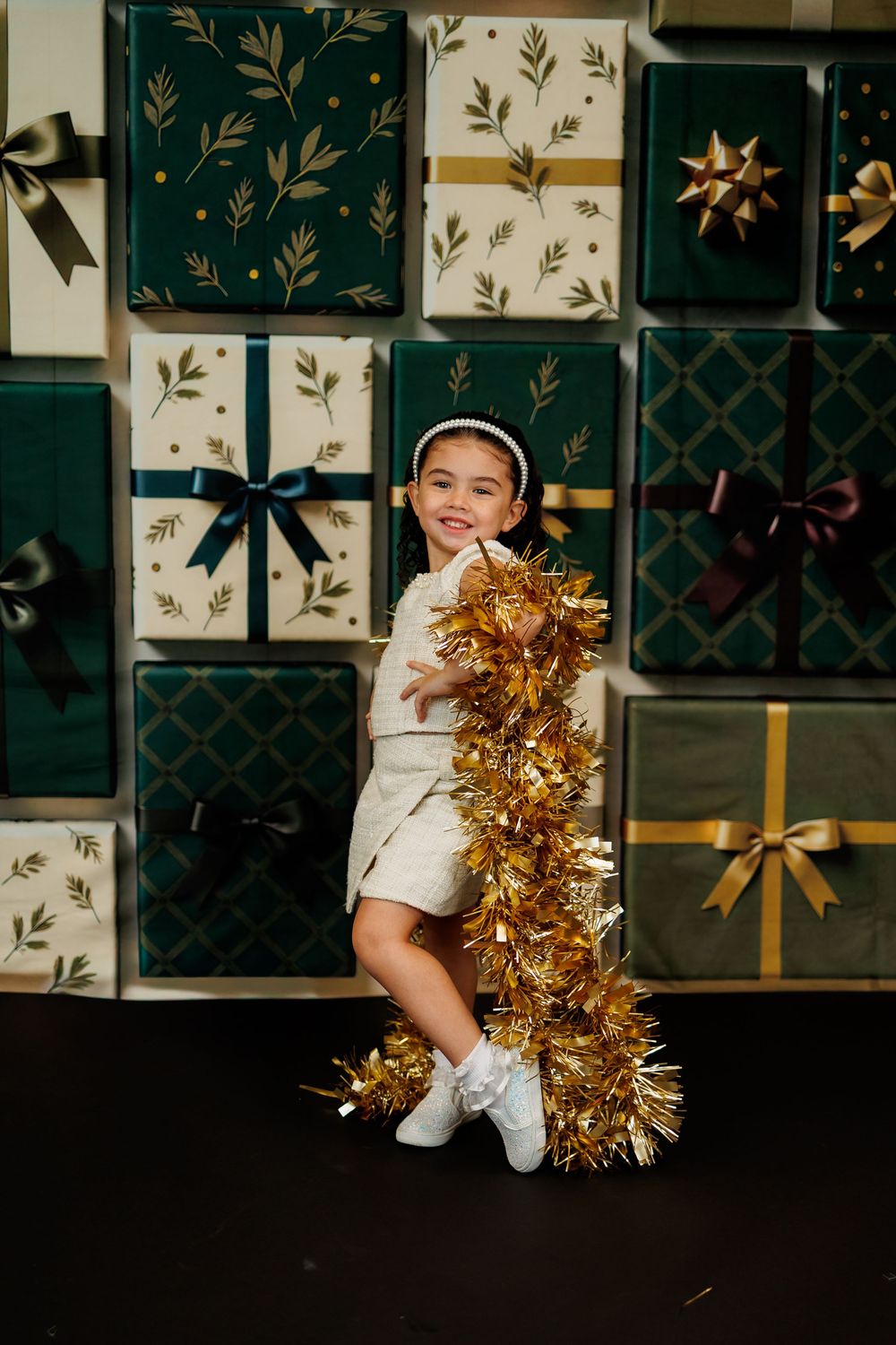 Cheerleader in white uniform with gold pom poms performs energetic dance moves against decorative wall backdrop.
