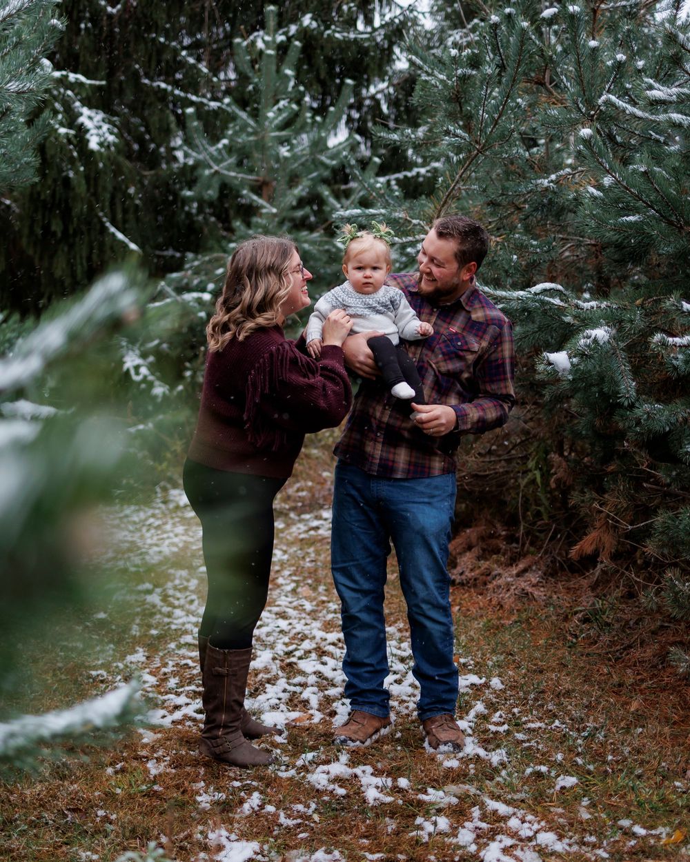 Family enjoying a winter moment together among snow-dusted evergreen trees on a forest path.